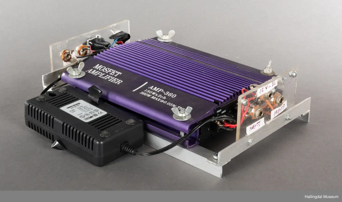 Hjemmelaget transportabelt lydanlegg. Rødbrun skinnkoffert med messingbeslag. Lysebrunt skinn innvendig fôr. Inneholder en ombygd "Mosfet" amplifier i lilla farge, med tilhørende grå strømkabel. På sidene er det plexiglass. Høyre side plexiglass bestående av strøminntak kontakt og en av og på bryter og to stk. merket mikserinngang til jack. På venstre side plexiglass inntak med merke: 12V - DG og to høytalerinnganger. Kabler til høytaler og mikrofon mangler.  