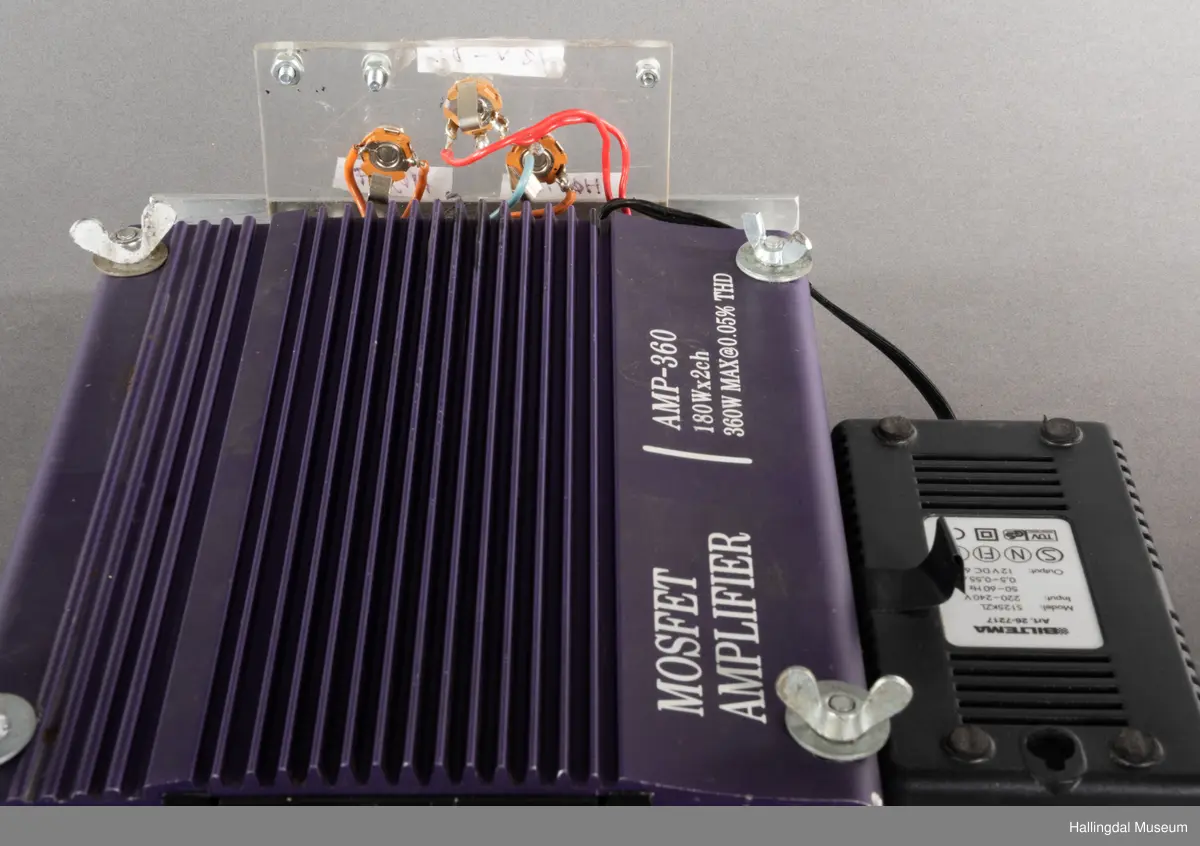 Hjemmelaget transportabelt lydanlegg. Rødbrun skinnkoffert med messingbeslag. Lysebrunt skinn innvendig fôr. Inneholder en ombygd "Mosfet" amplifier i lilla farge, med tilhørende grå strømkabel. På sidene er det plexiglass. Høyre side plexiglass bestående av strøminntak kontakt og en av og på bryter og to stk. merket mikserinngang til jack. På venstre side plexiglass inntak med merke: 12V - DG og to høytalerinnganger. Kabler til høytaler og mikrofon mangler.  