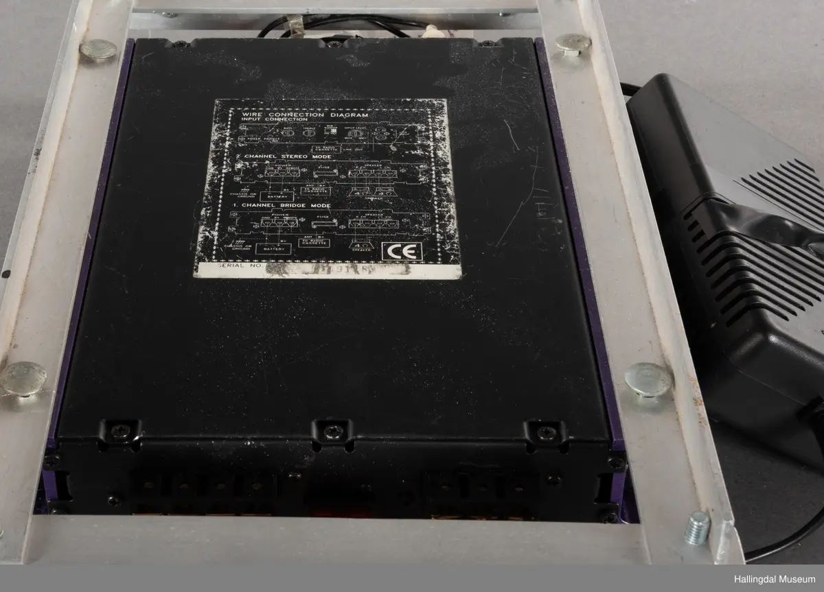 Hjemmelaget transportabelt lydanlegg. Rødbrun skinnkoffert med messingbeslag. Lysebrunt skinn innvendig fôr. Inneholder en ombygd "Mosfet" amplifier i lilla farge, med tilhørende grå strømkabel. På sidene er det plexiglass. Høyre side plexiglass bestående av strøminntak kontakt og en av og på bryter og to stk. merket mikserinngang til jack. På venstre side plexiglass inntak med merke: 12V - DG og to høytalerinnganger. Kabler til høytaler og mikrofon mangler.  