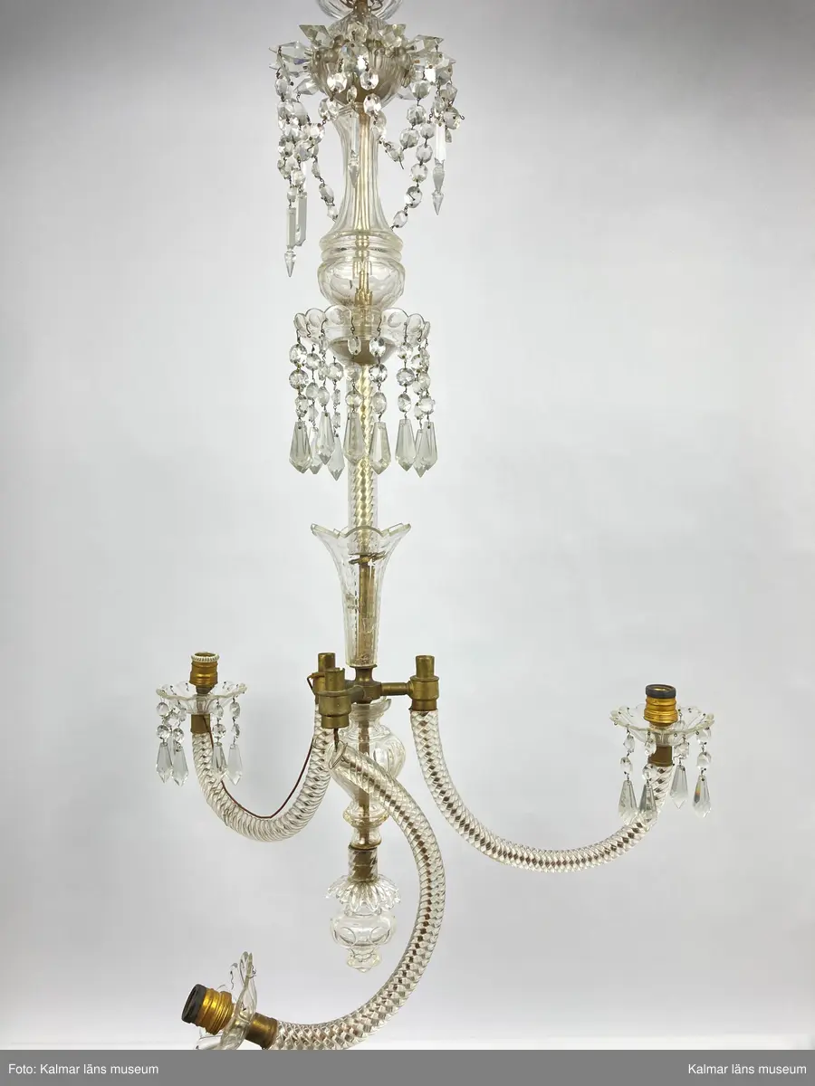 KLM 46969:3. Ljuskrona. Venetiansk stil. Stomme av mässing, övriga detaljer av slipat glas i olika former. Elektrifierad. Till ljuskronan hör diverse lösa delar, se KLM 46969:4.