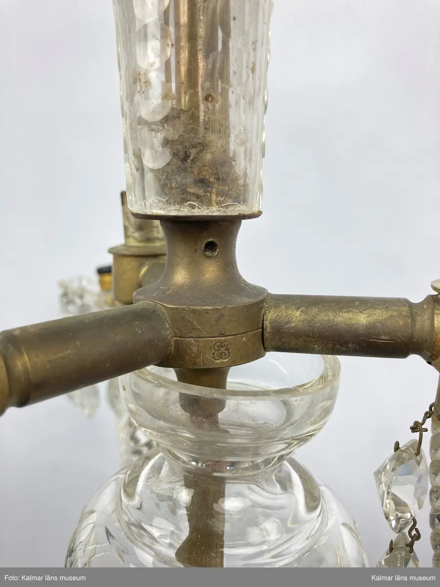 KLM 46969:1. Ljuskrona. Venetiansk stil. Stomme av mässing, övriga detaljer av slipat glas i olika former. Elektrifierad. På metallstommen en stämpel: EP. Till ljuskronan hör diverse lösa delar, se KLM 46969:4.