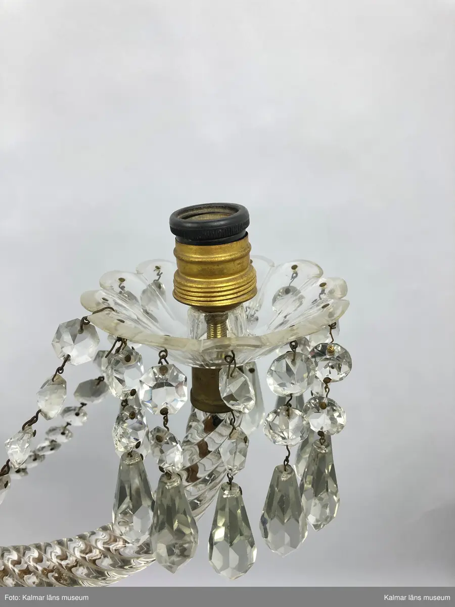 KLM 46969:1. Ljuskrona. Venetiansk stil. Stomme av mässing, övriga detaljer av slipat glas i olika former. Elektrifierad. På metallstommen en stämpel: EP. Till ljuskronan hör diverse lösa delar, se KLM 46969:4.