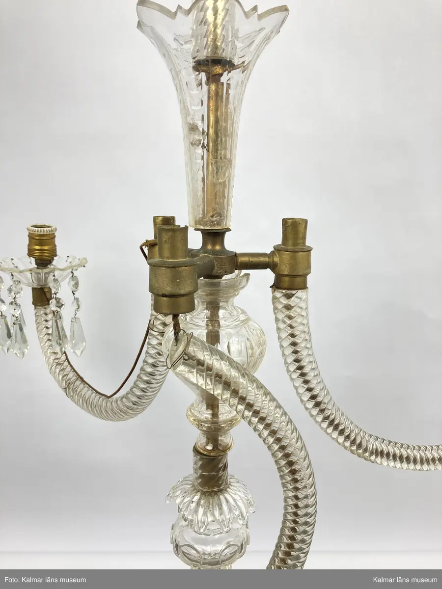 KLM 46969:3. Ljuskrona. Venetiansk stil. Stomme av mässing, övriga detaljer av slipat glas i olika former. Elektrifierad. Till ljuskronan hör diverse lösa delar, se KLM 46969:4.