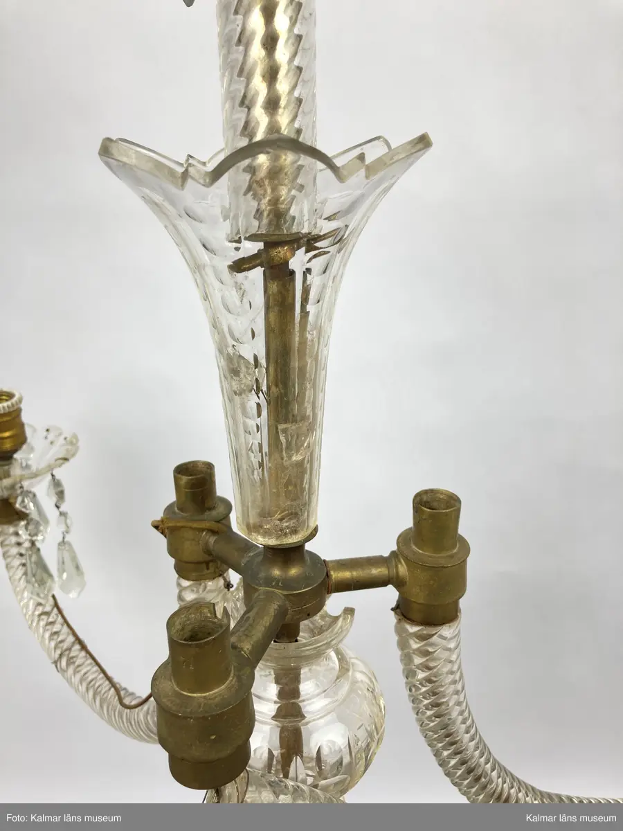 KLM 46969:3. Ljuskrona. Venetiansk stil. Stomme av mässing, övriga detaljer av slipat glas i olika former. Elektrifierad. Till ljuskronan hör diverse lösa delar, se KLM 46969:4.