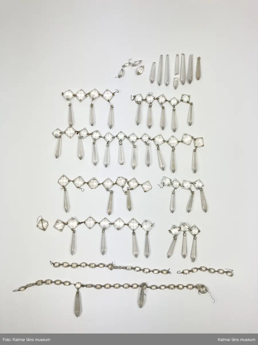 KLM 46968. Ljuskrona. Stomme av metall och trä med löstagbara ljusarmar av spiralvridet glas. Även löstagbara metallbågar med prismor. Nedre glaspartiet belagt med guldfärg på insidan. Prismor av slipat glas, flertalet lösa och osäkert hur de har suttit. Ena ljusarmen har en äldre lagning.