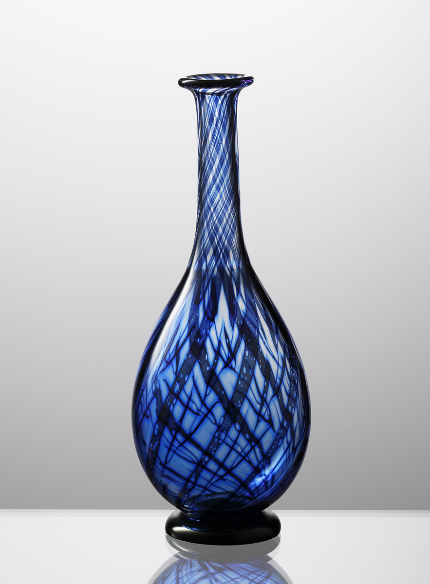 Graalvas, droppformad med utvikt mynningskant och svart låg fot.
Växtmönster i dunkelblå nyanser mot klar bakgrund.
Formgivare: Eva Englund.