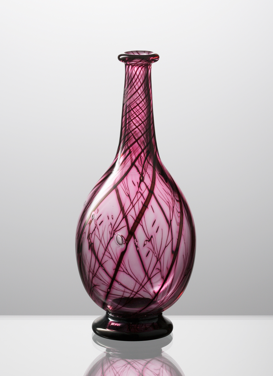 Graalvas, droppformad med utvikt mynningskant och svart låg fot.
Växtmönster i rubinröda nyanser mot violett bakgrund.
Formgivare: Eva Englund.