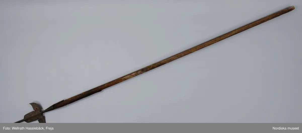 Kataloglappen:
"Korsgevär av järn och trä. Pikudden tveeggad, lancettlik; det bredare mellanpartiet saknar den sedvanliga åsen längs mittpartiet. Skaftstången alldeles rund. Skaftet av björk, grönmålad". 

I jämförelse med liknande korsgevär ser man att det inte är tillverkat vid någon av faktorierna utan resultatet av en lokal smeds försök att efterlikna förlagan men glömmt de nödvändiga detaljarbetet. Korsgeväret har med all sannorlikhet använts vid officiella tillfällen i Skänninge , från 1780 -talet fram till 1880-talets början.
/Johan Åkerlund 2006