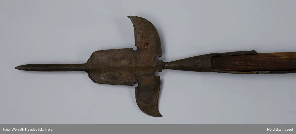 Kataloglappen:
"Korsgevär av järn och trä. Pikudden tveeggad, lancettlik; det bredare mellanpartiet saknar den sedvanliga åsen längs mittpartiet. Skaftstången alldeles rund. Skaftet av björk, grönmålad". 

I jämförelse med liknande korsgevär ser man att det inte är tillverkat vid någon av faktorierna utan resultatet av en lokal smeds försök att efterlikna förlagan men glömmt de nödvändiga detaljarbetet. Korsgeväret har med all sannorlikhet använts vid officiella tillfällen i Skänninge , från 1780 -talet fram till 1880-talets början.
/Johan Åkerlund 2006