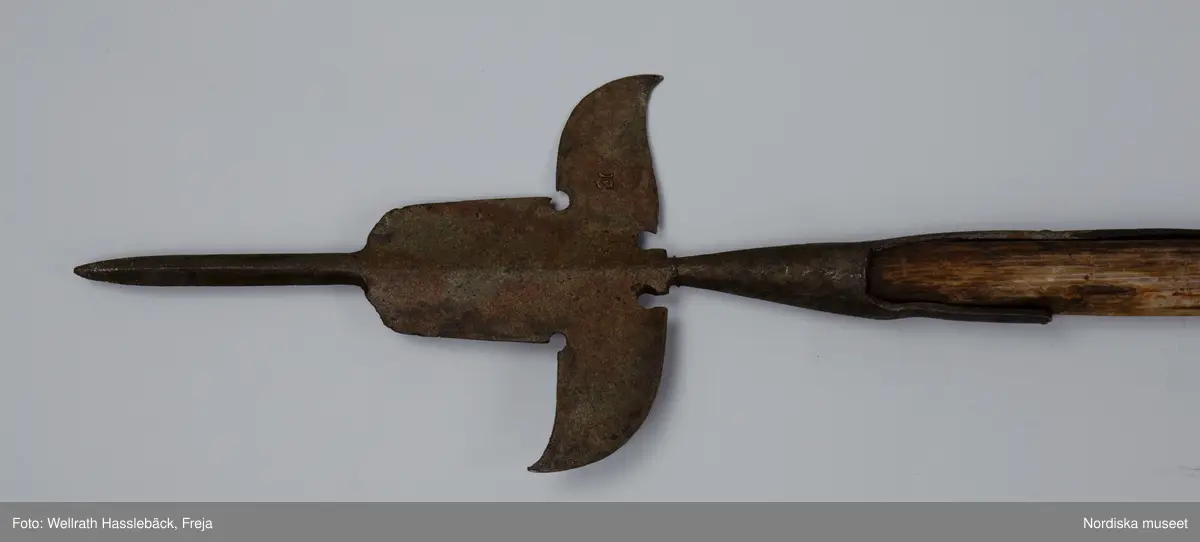 Kataloglappen:
"Korsgevär av järn och trä. Pikudden tveeggad, lancettlik; det bredare mellanpartiet saknar den sedvanliga åsen längs mittpartiet. Skaftstången alldeles rund. Skaftet av björk, grönmålad". 

I jämförelse med liknande korsgevär ser man att det inte är tillverkat vid någon av faktorierna utan resultatet av en lokal smeds försök att efterlikna förlagan men glömmt de nödvändiga detaljarbetet. Korsgeväret har med all sannorlikhet använts vid officiella tillfällen i Skänninge , från 1780 -talet fram till 1880-talets början.
/Johan Åkerlund 2006