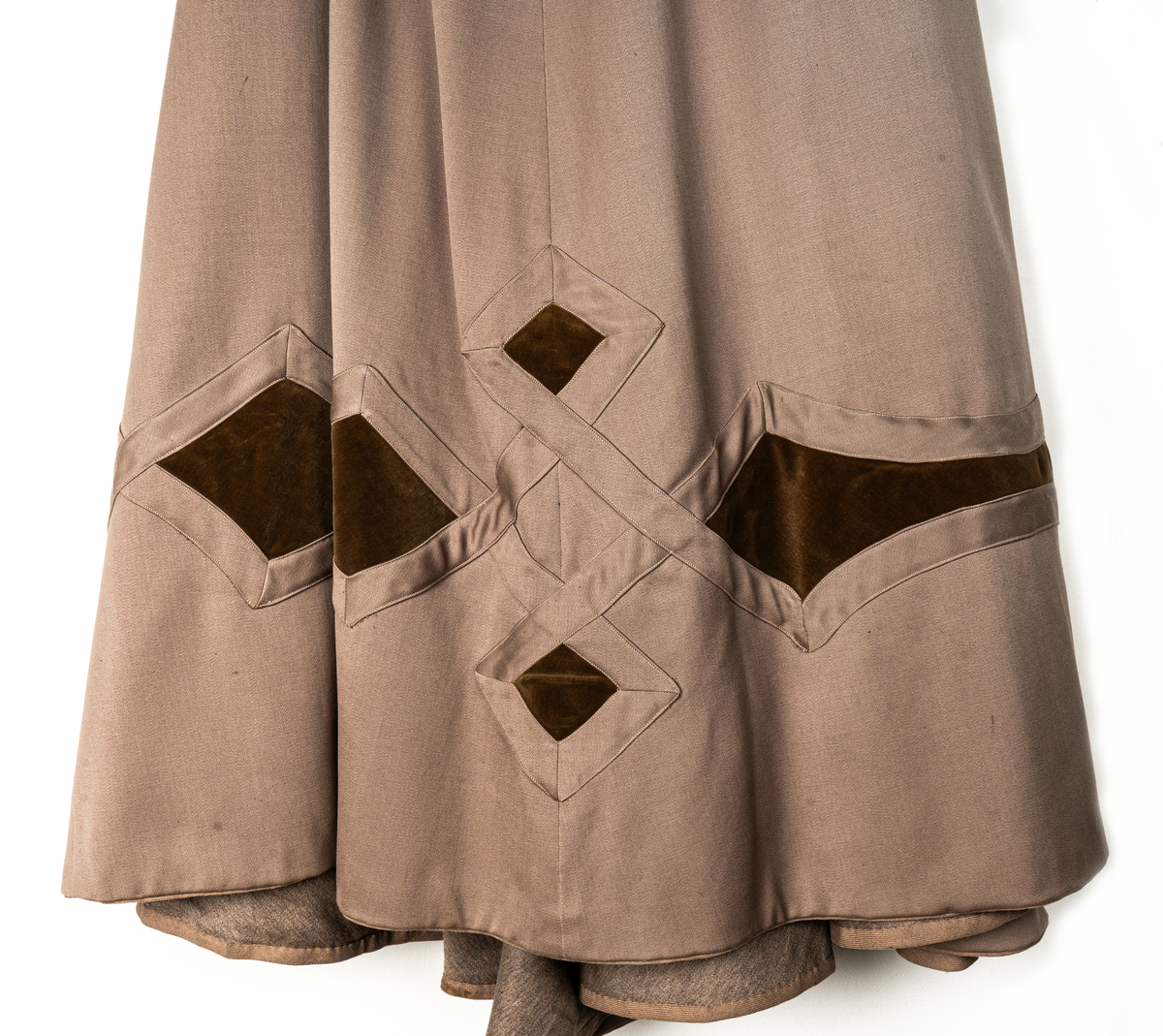 Klänning, beige yllegabardin och olivgrön sammet.
a) Kjol, klockad gabardin. Rutmönster nedtill med infällda sammetsfyrkanter. L 105cm.
b) Jacka, sammet. Krage och slag av gabardin med blommor av sammet. Knäppning fram. Långa puffärmar med slag. livet och ärmarna dekorerade med gabardinremsor. L fram 43cm, bak 37cm.
c) Väst, gabardin kantad med sammet. Urringad knäppning fram.
L fram 27cm, bak 18cm.