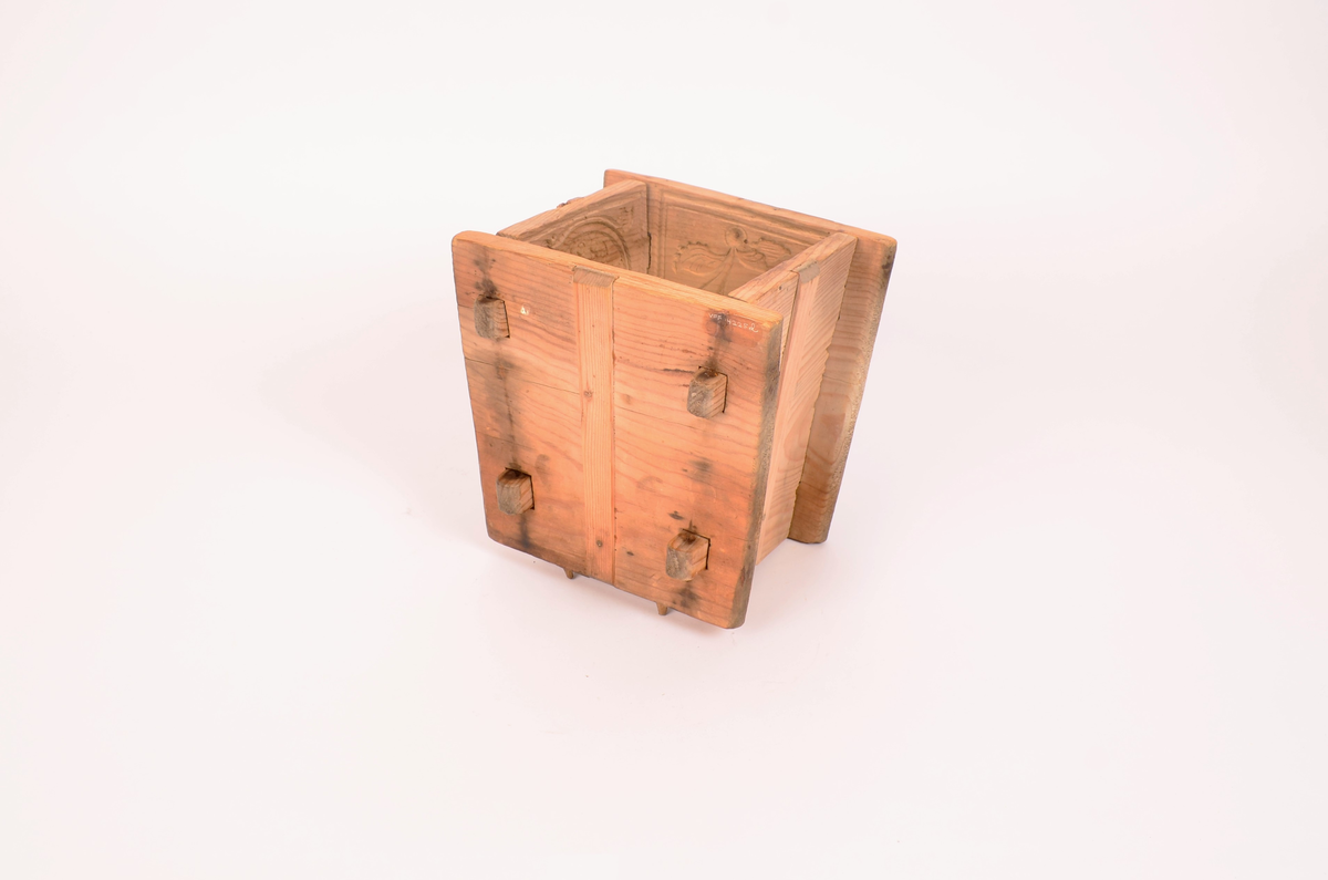 Gran, skåret. Fire sider, hver side trapesformet, skåret i et stykke og avstivet med stående labanker. To av sidene er skåret med to tapper på hver side med hull i. På de to andre, er skåret fire rektangulære hull (spalter), et i nærheten av hvert hjørne, som tappene passer inn i. Tappene settes inn i spaltene, og holdes på plass med sprosser. Sprossene mangler. I øvre kant på en av sidene er det kilt inn tilsammen tre tapper til feste for formens lokk ("tak"?). En tapp og lokket mangler. Skåret dekor på hver side.