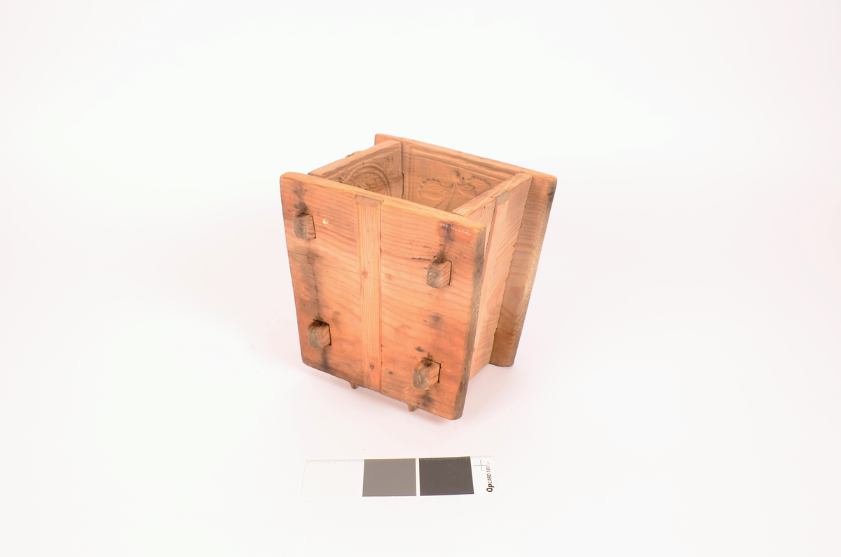 Gran, skåret. Fire sider, hver side trapesformet, skåret i et stykke og avstivet med stående labanker. To av sidene er skåret med to tapper på hver side med hull i. På de to andre, er skåret fire rektangulære hull (spalter), et i nærheten av hvert hjørne, som tappene passer inn i. Tappene settes inn i spaltene, og holdes på plass med sprosser. Sprossene mangler. I øvre kant på en av sidene er det kilt inn tilsammen tre tapper til feste for formens lokk ("tak"?). En tapp og lokket mangler. Skåret dekor på hver side.