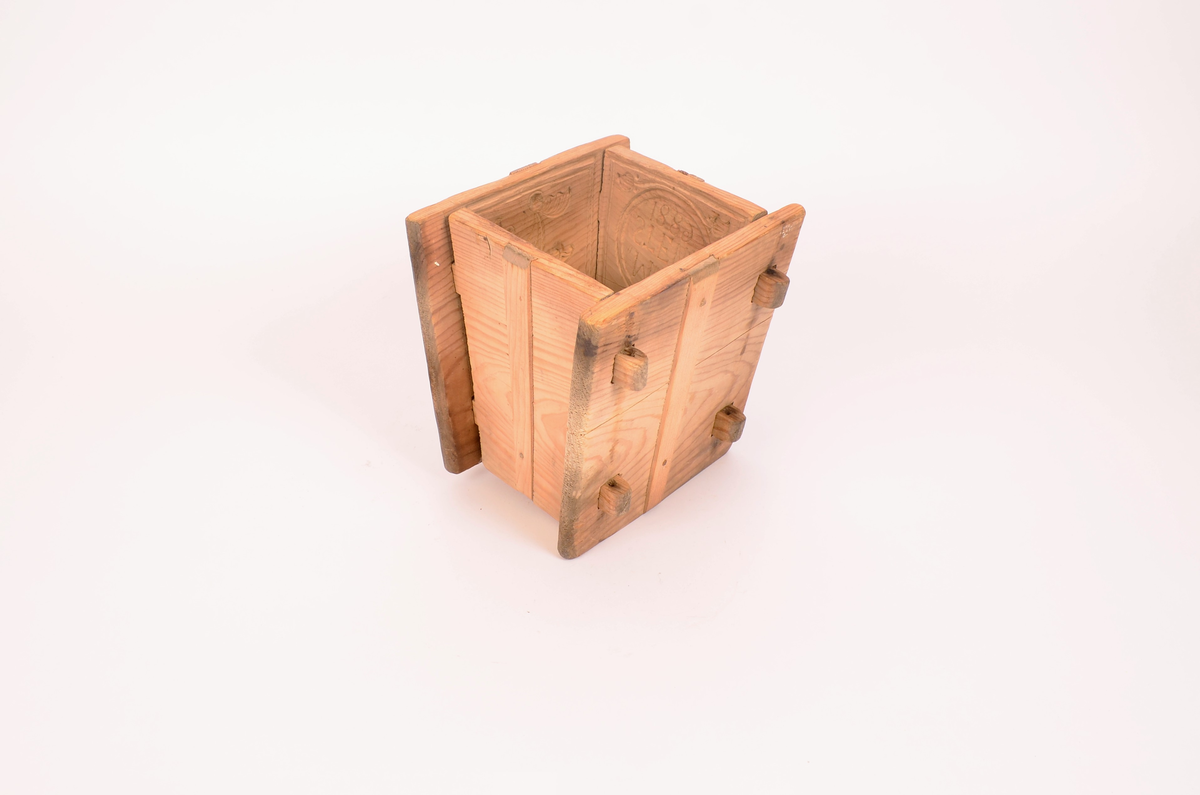 Gran, skåret. Fire sider, hver side trapesformet, skåret i et stykke og avstivet med stående labanker. To av sidene er skåret med to tapper på hver side med hull i. På de to andre, er skåret fire rektangulære hull (spalter), et i nærheten av hvert hjørne, som tappene passer inn i. Tappene settes inn i spaltene, og holdes på plass med sprosser. Sprossene mangler. I øvre kant på en av sidene er det kilt inn tilsammen tre tapper til feste for formens lokk ("tak"?). En tapp og lokket mangler. Skåret dekor på hver side.