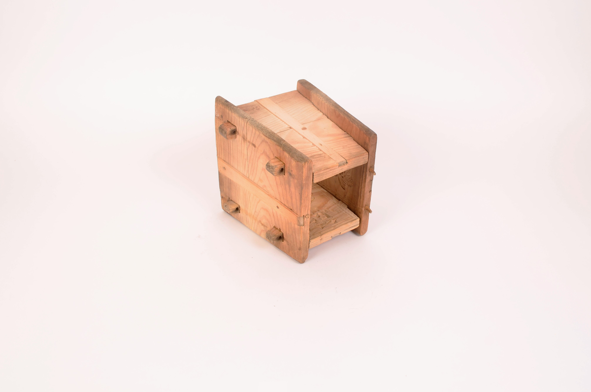 Gran, skåret. Fire sider, hver side trapesformet, skåret i et stykke og avstivet med stående labanker. To av sidene er skåret med to tapper på hver side med hull i. På de to andre, er skåret fire rektangulære hull (spalter), et i nærheten av hvert hjørne, som tappene passer inn i. Tappene settes inn i spaltene, og holdes på plass med sprosser. Sprossene mangler. I øvre kant på en av sidene er det kilt inn tilsammen tre tapper til feste for formens lokk ("tak"?). En tapp og lokket mangler. Skåret dekor på hver side.