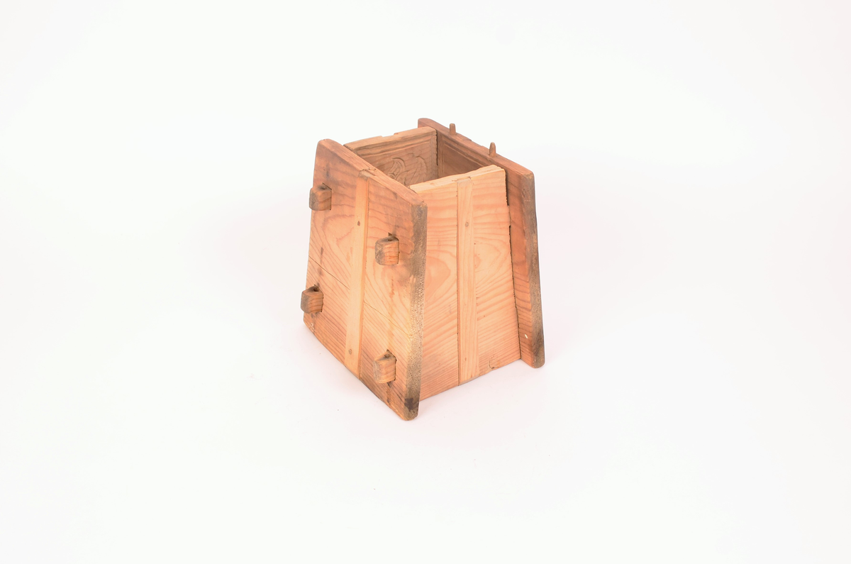 Gran, skåret. Fire sider, hver side trapesformet, skåret i et stykke og avstivet med stående labanker. To av sidene er skåret med to tapper på hver side med hull i. På de to andre, er skåret fire rektangulære hull (spalter), et i nærheten av hvert hjørne, som tappene passer inn i. Tappene settes inn i spaltene, og holdes på plass med sprosser. Sprossene mangler. I øvre kant på en av sidene er det kilt inn tilsammen tre tapper til feste for formens lokk ("tak"?). En tapp og lokket mangler. Skåret dekor på hver side.