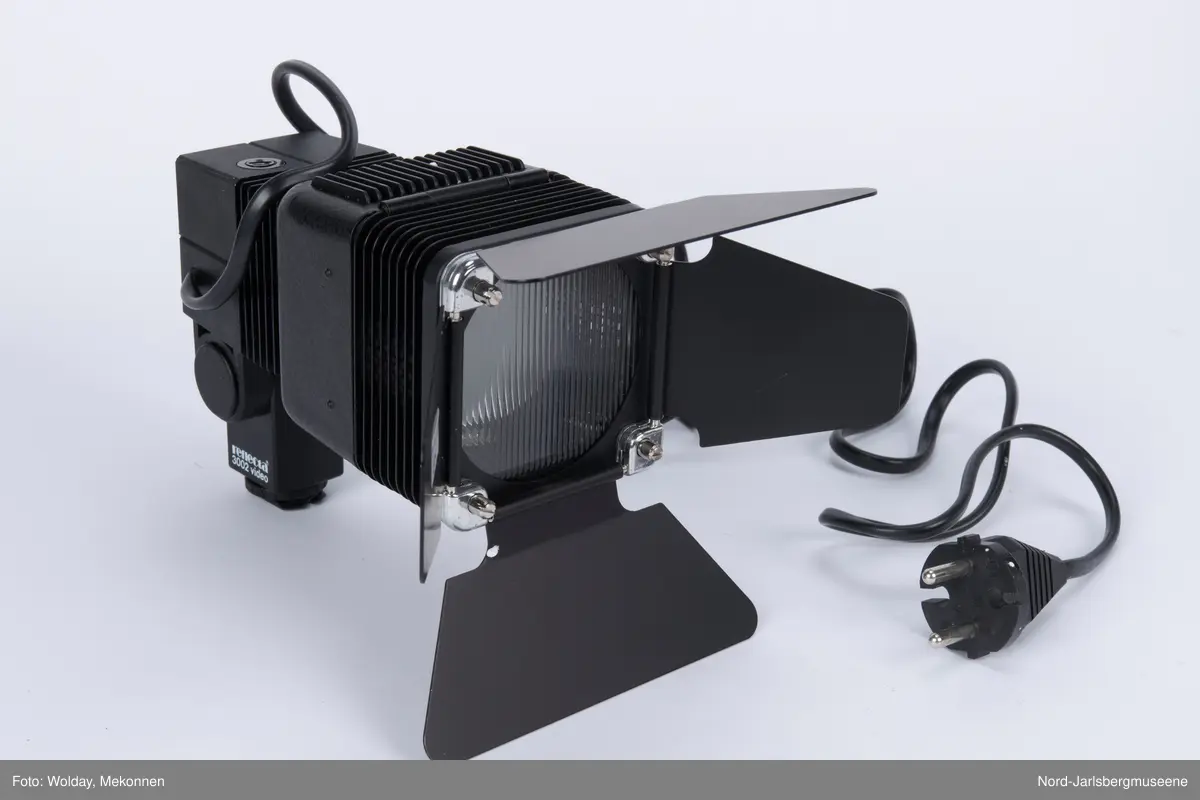 Videolys i original emballasje; isoporboks med pappomslag. Videolampen er i sort metall ledning, . Eske med ekstra halogenpærer medfølger (tom). Pappomslaget med foto av lampen invendig, med teknisk info.
Manual med veiledning på fire språk.