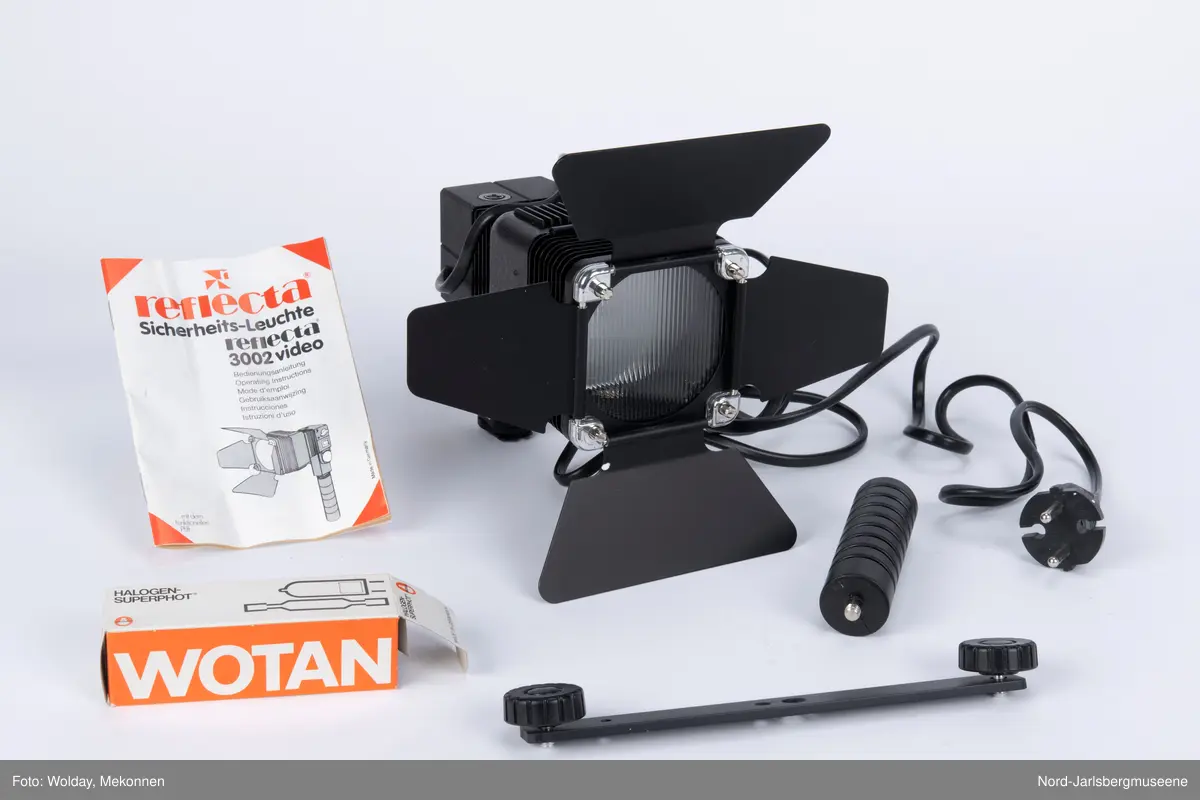 Videolys i original emballasje; isoporboks med pappomslag. Videolampen er i sort metall ledning, . Eske med ekstra halogenpærer medfølger (tom). Pappomslaget med foto av lampen invendig, med teknisk info.
Manual med veiledning på fire språk.