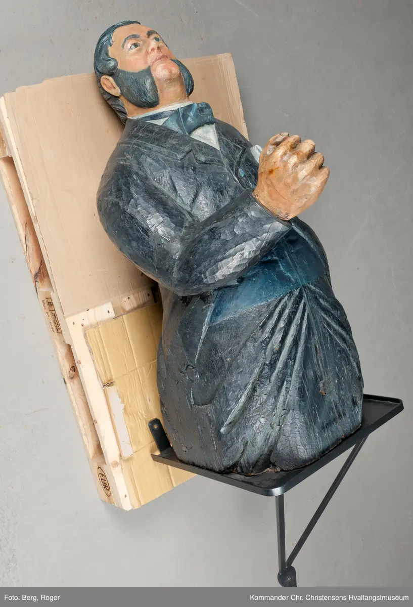 Sortkledd mann med stiv snipp. Bakkenbart, kinnskjegg uten forbindelse med hakeskjegg eller bart.