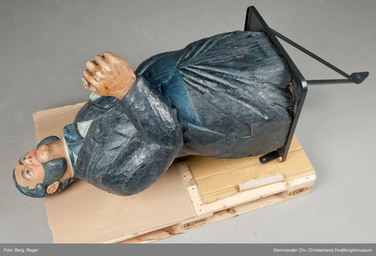 Sortkledd mann med stiv snipp. Bakkenbart, kinnskjegg uten forbindelse med hakeskjegg eller bart.