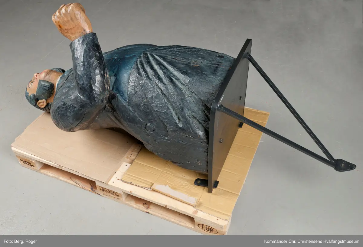 Sortkledd mann med stiv snipp. Bakkenbart, kinnskjegg uten forbindelse med hakeskjegg eller bart.