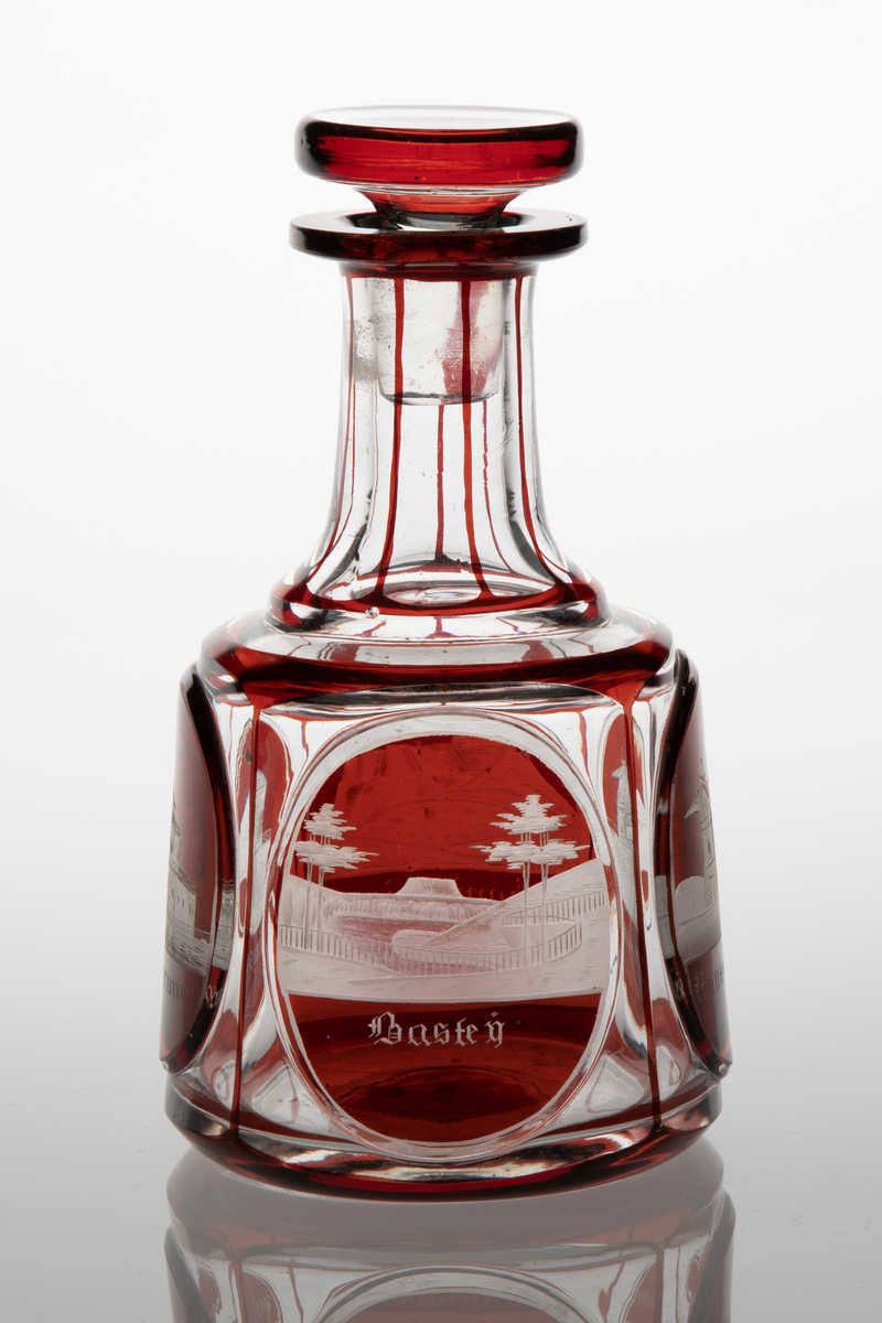 Karaffel med propp i klart glass med dekor i rødt overfang. Sylindrisk korpus med sider som skrår svakt innover. På korpus fire slipte fasetter, i hver fasett er ovalslipt medaljong, i disse gravert dekor i form av bygninger. Under respektive bygning står det: "Königsbrunn", "Basteÿ", "Winterberghaus" og "Königstein." Hals inndelt i sju seksjoner med hjelp av streker i rødt glass. Skiveformet rød propp.