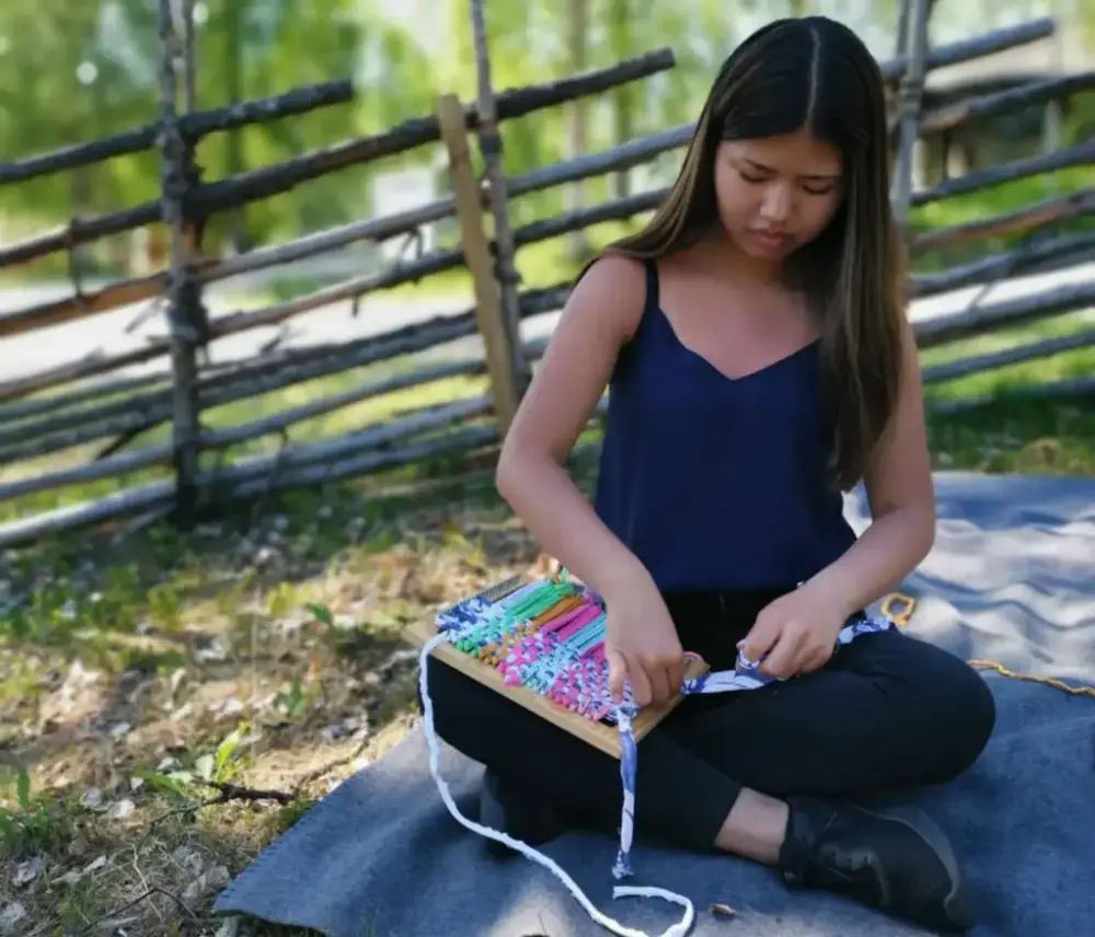 Flicka sitter på en filt i gräset och slöjdar