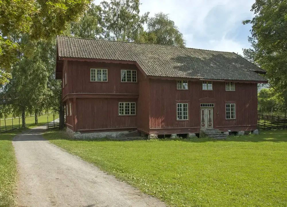 Rød, plankekledd bygning fra 160, med litt utstikkende andreetasje og innbygget svalgang som stikker ut. Smårutete vinduer og enkrums terrakottabrun takstein.