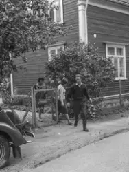 Mann med epler i eit nett på veg ut porten saman med to kvin