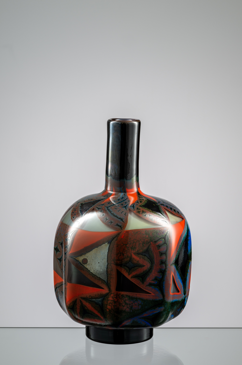 "Millefiori" Formgivare: Eva Englund. Graalvas, åttkantig rundad flaskform med svart fotklack. Grafisk dekor i röd och blå nyans mot mörk fond.