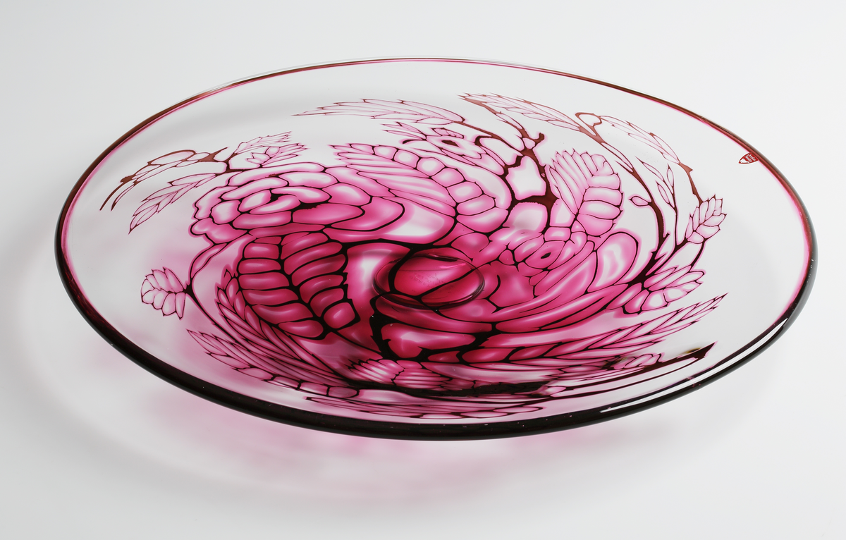 Graalfat, rund form med låg, klar fotklack. Dekor i form av växtmönster i rosa och svart nyans.
Rosa och svart rand runt brättets kant. 
Formgivare: Eva Englund.