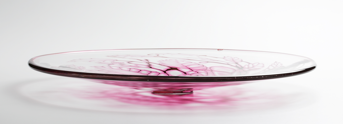 Graalfat, rund form med låg, klar fotklack. Dekor i form av växtmönster i rosa och svart nyans.
Rosa och svart rand runt brättets kant. 
Formgivare: Eva Englund.