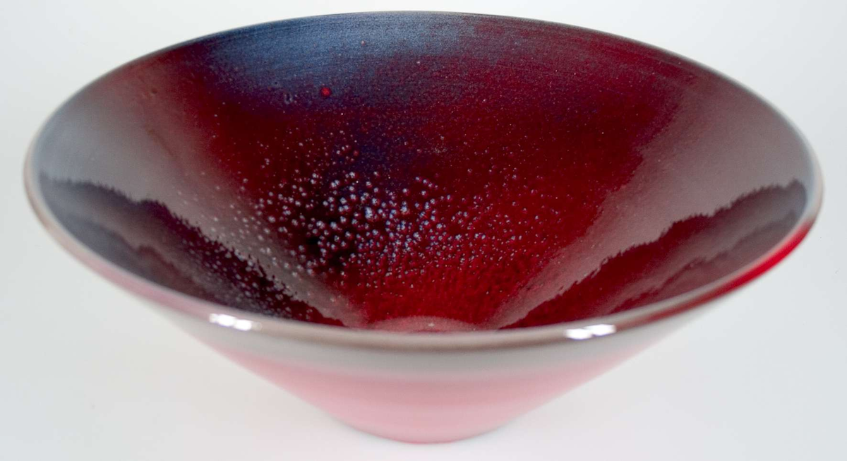 Skål av lergods, glaserad i mörkrött och gråblått. Flerskiktsglasyrer i violett, rött och blått. Signerad i massan: Atterberg 1970.
Enligt uppgift från Ingrid Atterberg har gas tillförts vid bränningen, så att mönster bildades på insidan av skålen. 