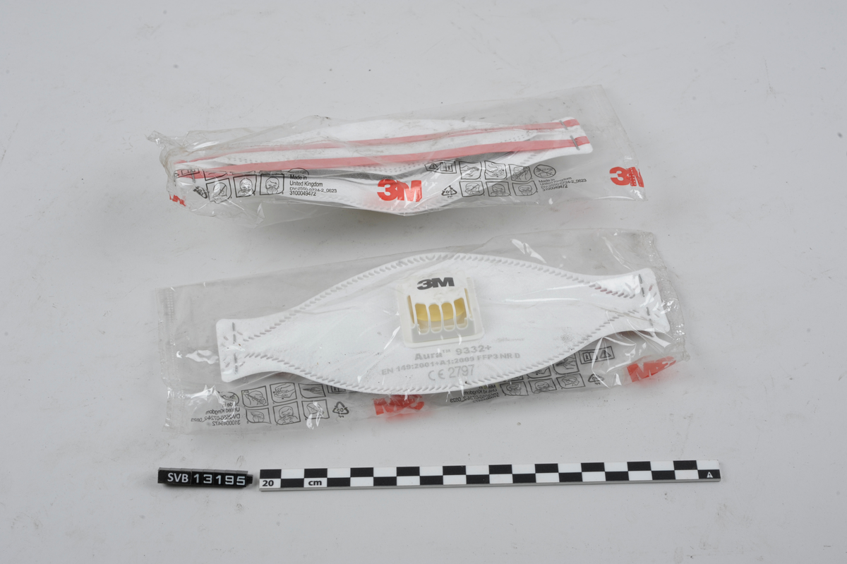 To støvmasker. Uåpnet, i plastemballasje. Maskene er av hvitt tøystoff. På baksiden er to røde stropper. På fronten er en hvit, firkantet ventil.