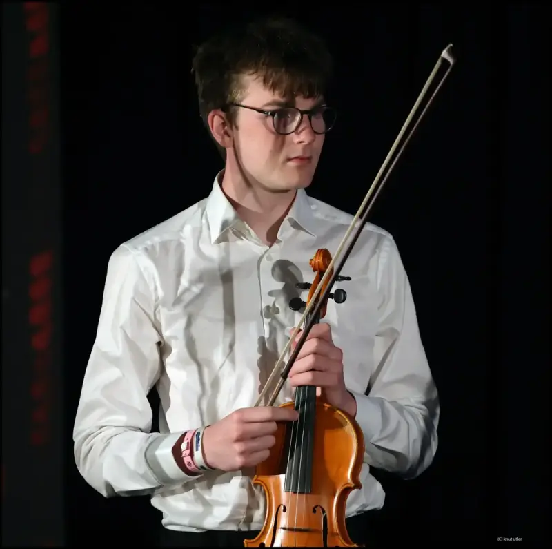 Jonathan Jansson i kvit skjorte held ei fele i eine handa og ei felebue i den andre