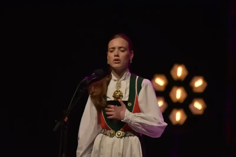 Felicia J. Storn i bunad står på ei scene og syng