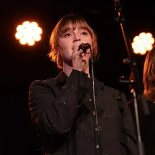 Lova Siverts i mørk skjorte står på ei scene og syng med ein mikrofon i handa