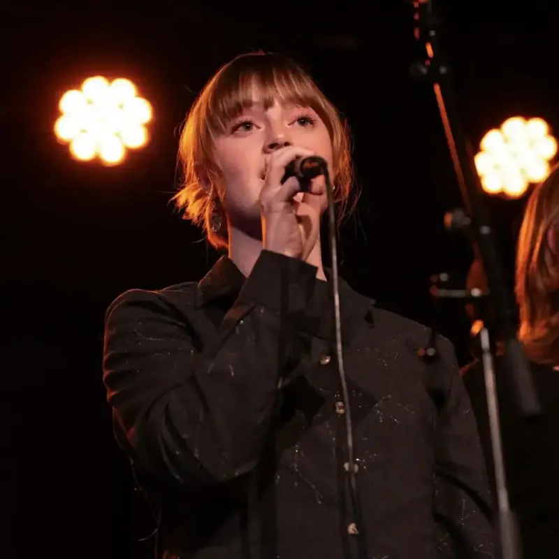 Lova Siverts i mørk skjorte står på ei scene og syng med ein mikrofon i handa