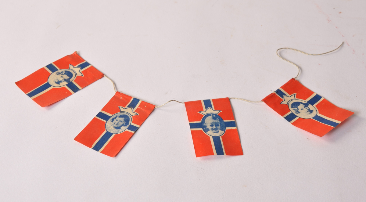 4 norske flagg av farget papir festet i hvitt snøre med lite bilde av kongelige barn i flaggets senter. De kongelige: Kong Harald 5, Prinsesse Ragnhild og Prinsesse Astrid.