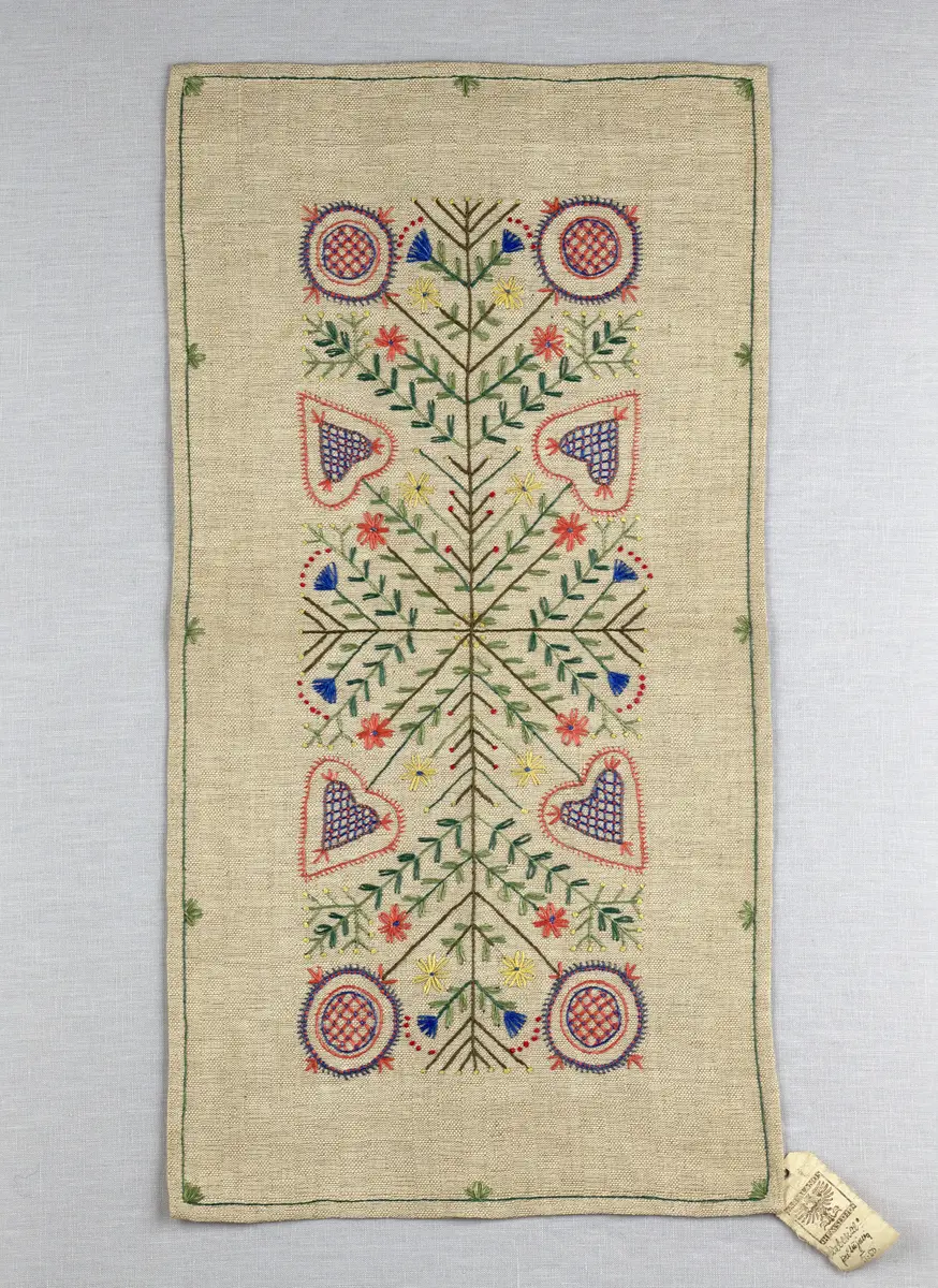 Löpare gjord av halvlinneväv i sålldräll och broderi utfört med lingarn i stjälksöm, läggsöm, langettsöm, oliksidig plattsöm, bottensöm samt knutar. 
Duken är inramad med en stjälksöm och har 7mm breda fållar runt om och raka hörn, som är sydda med kaststygn. 