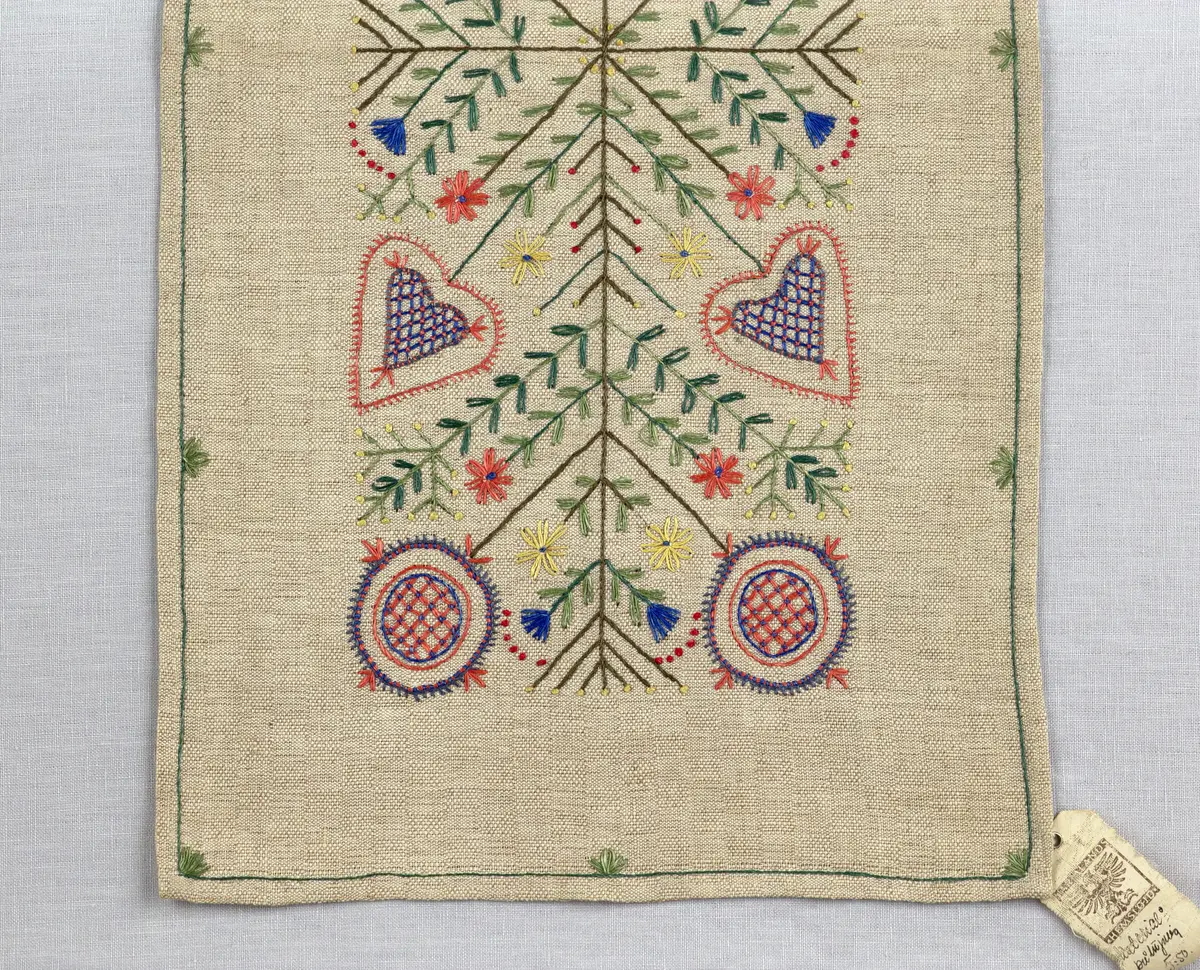 Löpare gjord av halvlinneväv i sålldräll och broderi utfört med lingarn i stjälksöm, läggsöm, langettsöm, oliksidig plattsöm, bottensöm samt knutar. 
Duken är inramad med en stjälksöm och har 7mm breda fållar runt om och raka hörn, som är sydda med kaststygn. 