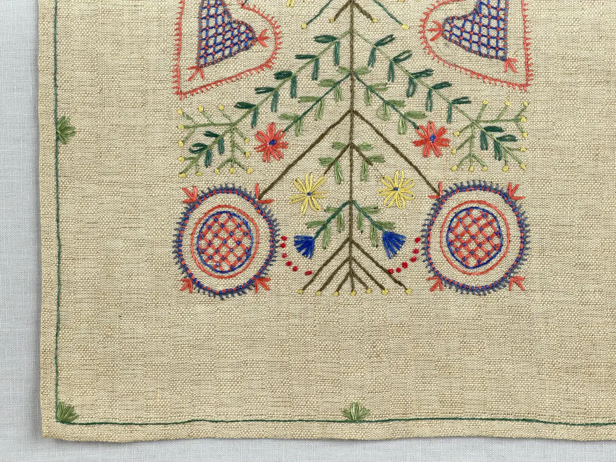 Löpare gjord av halvlinneväv i sålldräll och broderi utfört med lingarn i stjälksöm, läggsöm, langettsöm, oliksidig plattsöm, bottensöm samt knutar. 
Duken är inramad med en stjälksöm och har 7mm breda fållar runt om och raka hörn, som är sydda med kaststygn. 