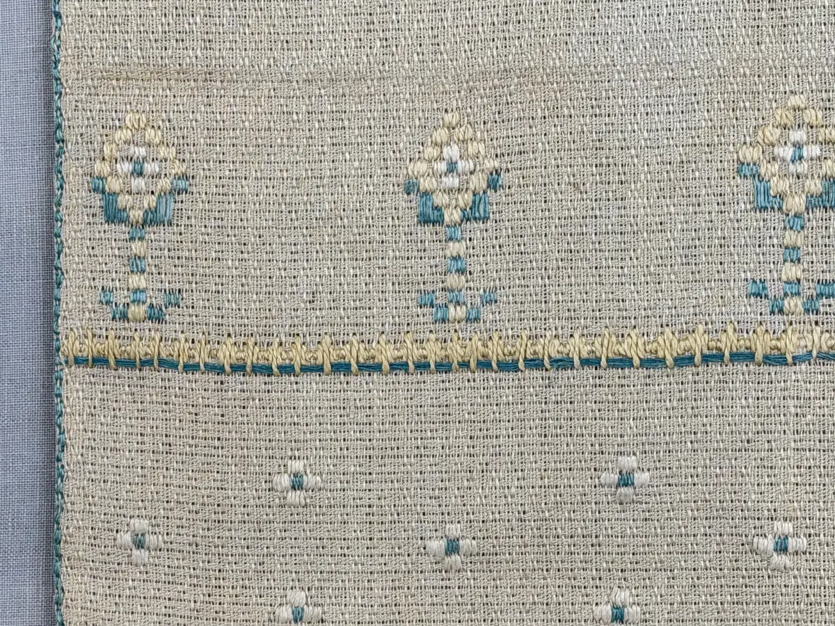 Löpare gjord av linneväv i sålldräll och broderi utfört med lingarn i plattsöm, flätsöm, trädstygn samt myrgång med tre kaststygn emellan. 
Långsidorna är kantade med efterstygn och duken har 6mm breda fållar runt om och raka hörn, som är sydda med smygstygn. 