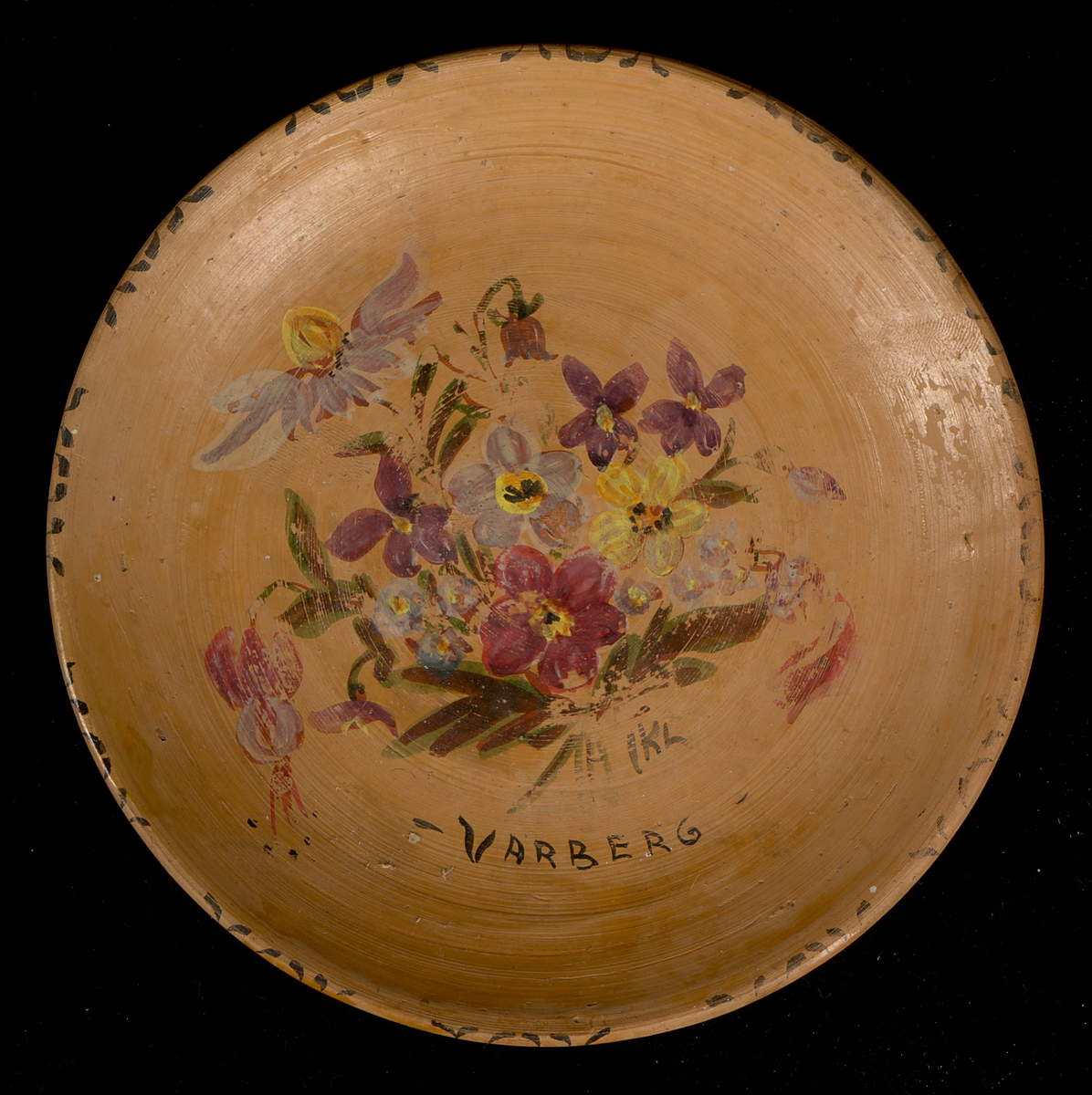 Prydnadsfat av lergods med handmålad blomsterdekor och texten "Varberg" i spegeln. Måleriet signerat: "IKL". Fatet är runt och svagt skålformat med låg kant. Tydliga drejspår samt fingeravtryck. Fatet bär en genomskinlig, mjölktonad glasyr, som ligger ovanpå dekoren. På undersidan av fatet finns en upphöjd fotring försedd med två hål för väggupphängning.

Signatur och årtal på undersidan: ”B(?)d.h. KIL. 75”. Även siffran ”3” skriven i blyerts.