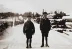 Thore Eriksson med lillebror Paul till vänster på vägen utanför sitt hem Solvik i Grimstorp, Nässjö kommun. Impregneringsstolpar till höger och samhället i fonden. Foto omkring 1930.