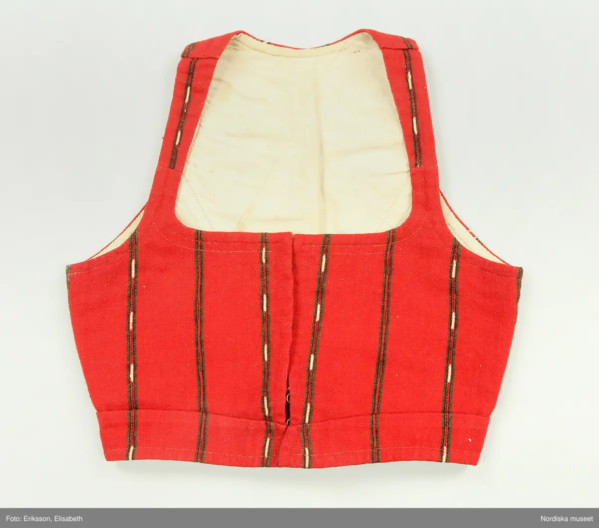 Huvudliggaren:
"Kvinnodräkt fr. Delsbo sn, Norra Helsinglands fgd, Helsingland.
a. "Ryntjeskjortel" af svart kläde med röd kant och bandväfd "kval" (linning). Kjolen "lurad"(goffrerad), skall förvaras lurad att ej vecken gå ut. 3 par fruntimmershänder hjälpas åt att "lura" den efter hvarje begagnande.
b. livstycke, rött med gröna ränder.
c. "Ryntjessärk" (rynksärk) af hvitt bomullstyg med "krus" (handbroderi) kring hals och händer.Begagnas sommartiden
d. "Bumsförkläde" af ylle, blårandigt med bandväf,"kval" i rödt och grönt.
e. "Förklesband" rödt och grönt ylle med "doppar" (tofsar) i ändarna. Lindas 1 à 2 hvarf kring lifvet och bindes framtill med stora nedhängande "locor" och ändar. Längd 262 cm, bredd 3,4 cm.
f. Kjolsäck med mässingslås och hake samt tennbroderi. Häktas under förklesbandet och hänger delvis under "försklet". Begagnas vanligen till förvaring af kyrkkryddor m.fl. kyrk-ellerkalassaker.
g. Halfhandskar af svart kläde med silkesbroderi. Begagnas sommartiden.
h. "Påshufva" hvardagsmössa af brokigt kattun. Begagnas med i nacken utslaget hår med några hårtestar hängande fritt framför öronen.
Till dräkten användes röda strumpor samt låga skor med höga klackar. Äfven kan användas silfersmycken kring halsen eller å  bröstet. En á två brokiga silkesdukar brukades omkring halsen nedstoppade under lifstycket, så att kruset kring halsen  på "ryntjessärken" sammanfästadt med ett löfspänne samt en smalare kant af hvarje sidenduk, blevo synliga. Vid handlederna sammanfästes ryntjessärken med röda sidenband eller länkknappar.

a. KJOL 
längd: 87 cm
midjeband bredd: 7 cm
av svart halvylle med svart linvarp och inslag av svart 1-tr. ullgarn, de 2 yttersta stadtrådarna är av oblekt lingarn. 4 goffrerade våder samt en slät framvåd som skarvats under förklädet med oblekt bomullslärft. 5 cm bred list av rött kläde i nederkanten runtom. Brett midjeband mönstervävt i rött och grönt ullgarn och vitt bomullsgarn. Knäppt vid framvådens vänstra sida med 2 hakar och hyskor av mässing.
b. LIVSTYCKE
längd: 39 cm
av halvylle i varptäckande kypert, varp av vitt lingarn, inslag av svart och grönt ullgarn med flaminslag av vitt, 2 fram-och sidstycken, 2 bakstycken avsmalnande till skörtveck med tre par tränsade förstärkningar av svart garn. I midjehöjd ett avsytt veck runtom, knäppt kant i kant med 8 par grova hakar och hyskor av mässing. Foder av ofärgad bomullslärft.
BE

c. ÖVERDEL
Längd: 39 cm. Längd: 58 cm - ärmlängd. Vidd: 56 cm - ärmvidd. Vidd: 114 cm. Höjd: 1,7 cm - kraghöjd. Material: Textil, bomull. Textil, linne - ärmlinning, krage. Bomullsgarn - broderi. Telnik: Tuskaft. Trådbundet broderi. Broderi, rätlinjig plattsöm. Handsömnad.
Överdel av tuskaftat vitt bomullstyg. Dubbelvikt bålstycke, isydda rektangulära halsspjäll. Täta breda stripade  rynkor mot halskrage i bomull, 1,7 cm hög. Kragen har broderier i rätlinjig plattsöm, vitt bomullsgarn över hela ytan, nuggor i kanten, langetterade bågar  i framkant. 16 cm långt sprund fram, tränsad förstärkning nedtill, 3 cm.  Vidsydd ärm med  infällda ärmspjäll, lagda veck över axeln fram och bak. Täta breda stripade rynkor mot 2,5 cm bred ärmlinning. Ärmlinningen har yttäckande vita broderier i rätlinjig plattsöm, rombiska former. Vita knytband i bomull i ärmlinningar och krage. Överdelen är handsydd.
/Inga-Lill Eliasson 2007-11-26


d. FÖRKLÄDE
längd=vådbredd: 82 cm
bredd: 97,5 cm
av halvylle, varp av svart lingarn, inslag i varptäckande kypert av svart 1-tr. ullgarn med smala ränder istarkt blått och en knappt synlig svart tråd med vita flamgarnsfläckar av bomull. Upptill stripade rynkor där de blå bårderna utnyttjats dekorativt i rynkningen. Mönstervävt midjeband i grönt på rött ullgarn , bandet knäpps med 2 hakar och hyskor i vänster sida.
I nederkantens båda hörn infodringar på insidan av svart bomullslärft, för att tyget inte skall rulla sig.



Berit Eldvik 2004