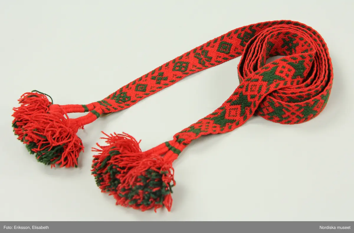 Huvudliggaren:
"Kvinnodräkt fr. Delsbo sn, Norra Helsinglands fgd, Helsingland.
a. "Ryntjeskjortel" af svart kläde med röd kant och bandväfd "kval" (linning). Kjolen "lurad"(goffrerad), skall förvaras lurad att ej vecken gå ut. 3 par fruntimmershänder hjälpas åt att "lura" den efter hvarje begagnande.
b. livstycke, rött med gröna ränder.
c. "Ryntjessärk" (rynksärk) af hvitt bomullstyg med "krus" (handbroderi) kring hals och händer.Begagnas sommartiden
d. "Bumsförkläde" af ylle, blårandigt med bandväf,"kval" i rödt och grönt.
e. "Förklesband" rödt och grönt ylle med "doppar" (tofsar) i ändarna. Lindas 1 à 2 hvarf kring lifvet och bindes framtill med stora nedhängande "locor" och ändar. Längd 262 cm, bredd 3,4 cm.
f. Kjolsäck med mässingslås och hake samt tennbroderi. Häktas under förklesbandet och hänger delvis under "försklet". Begagnas vanligen till förvaring af kyrkkryddor m.fl. kyrk-ellerkalassaker.
g. Halfhandskar af svart kläde med silkesbroderi. Begagnas sommartiden.
h. "Påshufva" hvardagsmössa af brokigt kattun. Begagnas med i nacken utslaget hår med några hårtestar hängande fritt framför öronen.
Till dräkten användes röda strumpor samt låga skor med höga klackar. Äfven kan användas silfersmycken kring halsen eller å  bröstet. En á två brokiga silkesdukar brukades omkring halsen nedstoppade under lifstycket, så att kruset kring halsen  på "ryntjessärken" sammanfästadt med ett löfspänne samt en smalare kant af hvarje sidenduk, blevo synliga. Vid handlederna sammanfästes ryntjessärken med röda sidenband eller länkknappar.

a. KJOL 
längd: 87 cm
midjeband bredd: 7 cm
av svart halvylle med svart linvarp och inslag av svart 1-tr. ullgarn, de 2 yttersta stadtrådarna är av oblekt lingarn. 4 goffrerade våder samt en slät framvåd som skarvats under förklädet med oblekt bomullslärft. 5 cm bred list av rött kläde i nederkanten runtom. Brett midjeband mönstervävt i rött och grönt ullgarn och vitt bomullsgarn. Knäppt vid framvådens vänstra sida med 2 hakar och hyskor av mässing.
b. LIVSTYCKE
längd: 39 cm
av halvylle i varptäckande kypert, varp av vitt lingarn, inslag av svart och grönt ullgarn med flaminslag av vitt, 2 fram-och sidstycken, 2 bakstycken avsmalnande till skörtveck med tre par tränsade förstärkningar av svart garn. I midjehöjd ett avsytt veck runtom, knäppt kant i kant med 8 par grova hakar och hyskor av mässing. Foder av ofärgad bomullslärft.
BE

c. ÖVERDEL
Längd: 39 cm. Längd: 58 cm - ärmlängd. Vidd: 56 cm - ärmvidd. Vidd: 114 cm. Höjd: 1,7 cm - kraghöjd. Material: Textil, bomull. Textil, linne - ärmlinning, krage. Bomullsgarn - broderi. Telnik: Tuskaft. Trådbundet broderi. Broderi, rätlinjig plattsöm. Handsömnad.
Överdel av tuskaftat vitt bomullstyg. Dubbelvikt bålstycke, isydda rektangulära halsspjäll. Täta breda stripade  rynkor mot halskrage i bomull, 1,7 cm hög. Kragen har broderier i rätlinjig plattsöm, vitt bomullsgarn över hela ytan, nuggor i kanten, langetterade bågar  i framkant. 16 cm långt sprund fram, tränsad förstärkning nedtill, 3 cm.  Vidsydd ärm med  infällda ärmspjäll, lagda veck över axeln fram och bak. Täta breda stripade rynkor mot 2,5 cm bred ärmlinning. Ärmlinningen har yttäckande vita broderier i rätlinjig plattsöm, rombiska former. Vita knytband i bomull i ärmlinningar och krage. Överdelen är handsydd.
/Inga-Lill Eliasson 2007-11-26


d. FÖRKLÄDE
längd=vådbredd: 82 cm
bredd: 97,5 cm
av halvylle, varp av svart lingarn, inslag i varptäckande kypert av svart 1-tr. ullgarn med smala ränder istarkt blått och en knappt synlig svart tråd med vita flamgarnsfläckar av bomull. Upptill stripade rynkor där de blå bårderna utnyttjats dekorativt i rynkningen. Mönstervävt midjeband i grönt på rött ullgarn , bandet knäpps med 2 hakar och hyskor i vänster sida.
I nederkantens båda hörn infodringar på insidan av svart bomullslärft, för att tyget inte skall rulla sig.



Berit Eldvik 2004