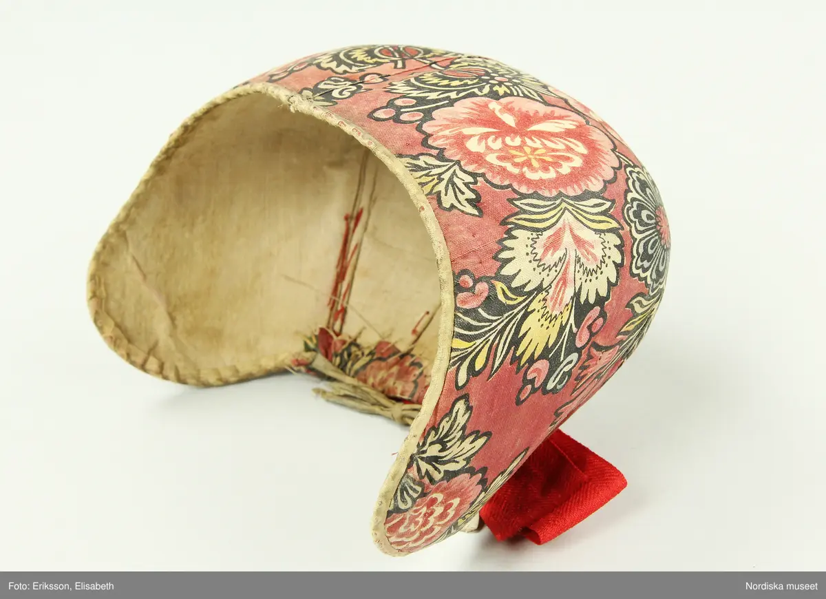 Huvudliggaren:
"Kvinnodräkt fr. Delsbo sn, Norra Helsinglands fgd, Helsingland.
a. "Ryntjeskjortel" af svart kläde med röd kant och bandväfd "kval" (linning). Kjolen "lurad"(goffrerad), skall förvaras lurad att ej vecken gå ut. 3 par fruntimmershänder hjälpas åt att "lura" den efter hvarje begagnande.
b. livstycke, rött med gröna ränder.
c. "Ryntjessärk" (rynksärk) af hvitt bomullstyg med "krus" (handbroderi) kring hals och händer.Begagnas sommartiden
d. "Bumsförkläde" af ylle, blårandigt med bandväf,"kval" i rödt och grönt.
e. "Förklesband" rödt och grönt ylle med "doppar" (tofsar) i ändarna. Lindas 1 à 2 hvarf kring lifvet och bindes framtill med stora nedhängande "locor" och ändar. Längd 262 cm, bredd 3,4 cm.
f. Kjolsäck med mässingslås och hake samt tennbroderi. Häktas under förklesbandet och hänger delvis under "försklet". Begagnas vanligen till förvaring af kyrkkryddor m.fl. kyrk-ellerkalassaker.
g. Halfhandskar af svart kläde med silkesbroderi. Begagnas sommartiden.
h. "Påshufva" hvardagsmössa af brokigt kattun. Begagnas med i nacken utslaget hår med några hårtestar hängande fritt framför öronen.
Till dräkten användes röda strumpor samt låga skor med höga klackar. Äfven kan användas silfersmycken kring halsen eller å  bröstet. En á två brokiga silkesdukar brukades omkring halsen nedstoppade under lifstycket, så att kruset kring halsen  på "ryntjessärken" sammanfästadt med ett löfspänne samt en smalare kant af hvarje sidenduk, blevo synliga. Vid handlederna sammanfästes ryntjessärken med röda sidenband eller länkknappar.