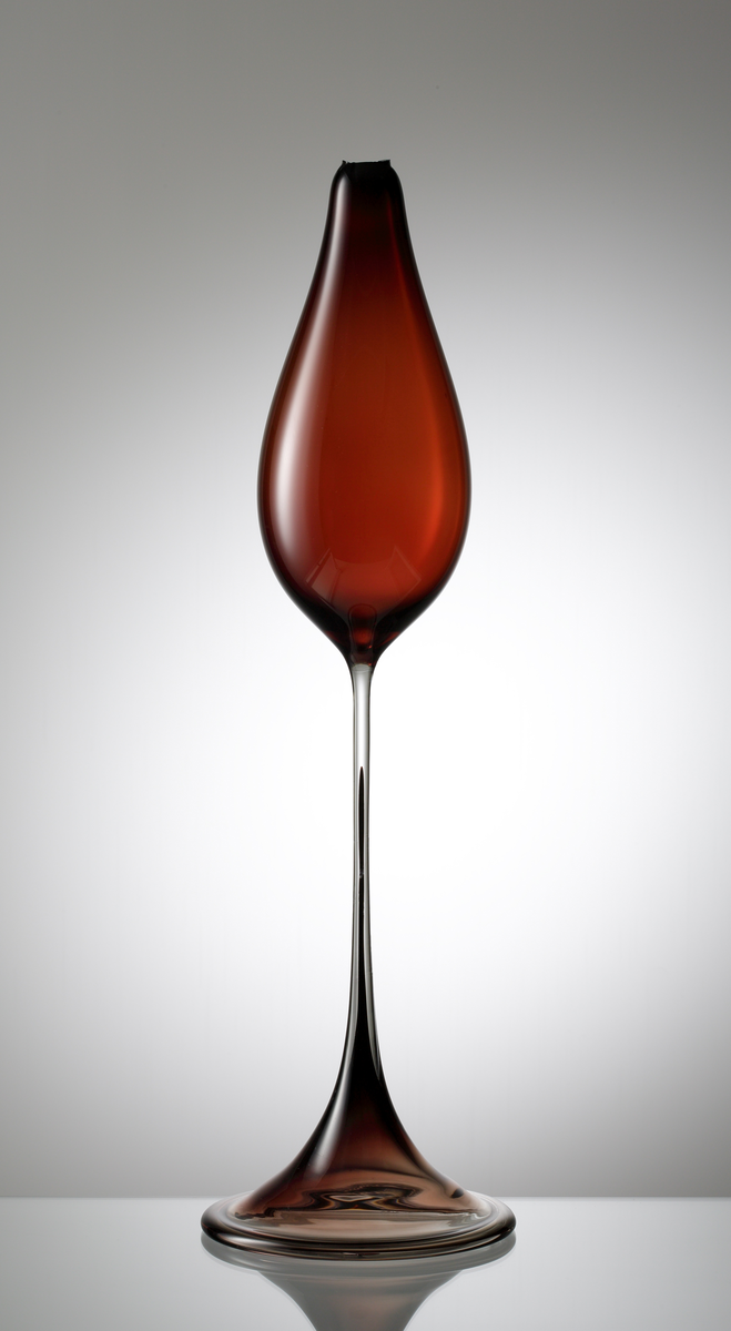 Formgivare: Nils Landberg. Tulpanvas i rödbrunfärgat underfång. Dropp formad kupa med draget högt ben. Utsvängd fot med omvikt kant och mörk rand. (Vass mynningskant, ej färdigställd).