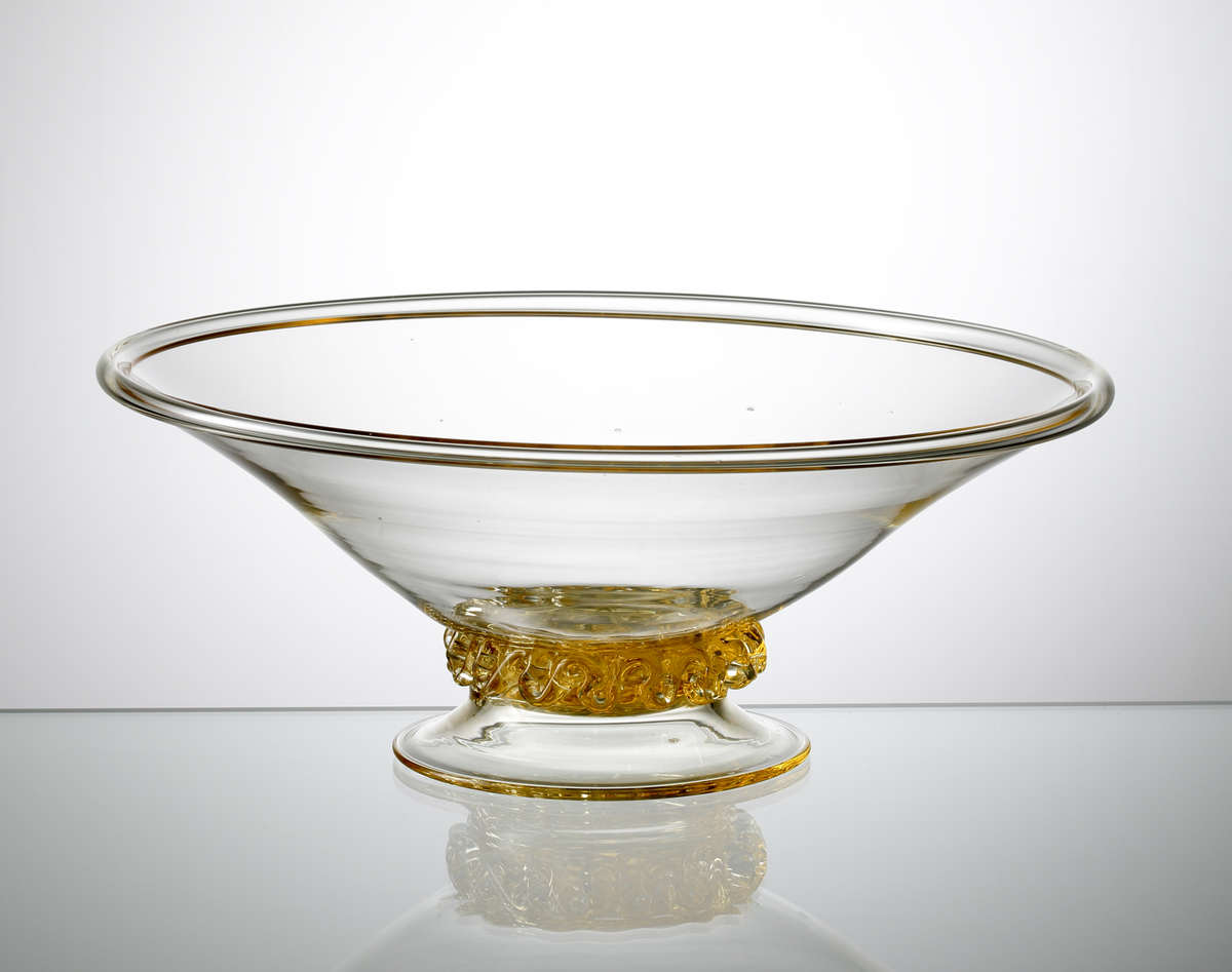 Formgivare: Nils Landberg. Skål på fot i gultonat glas. Klockformad kupa med omvikt mynningskant. Veckat band mellan skål och fot.
Ref: Gustav Abels del 2: "Landberg omkring 1945. Ett mindre antal sålda".